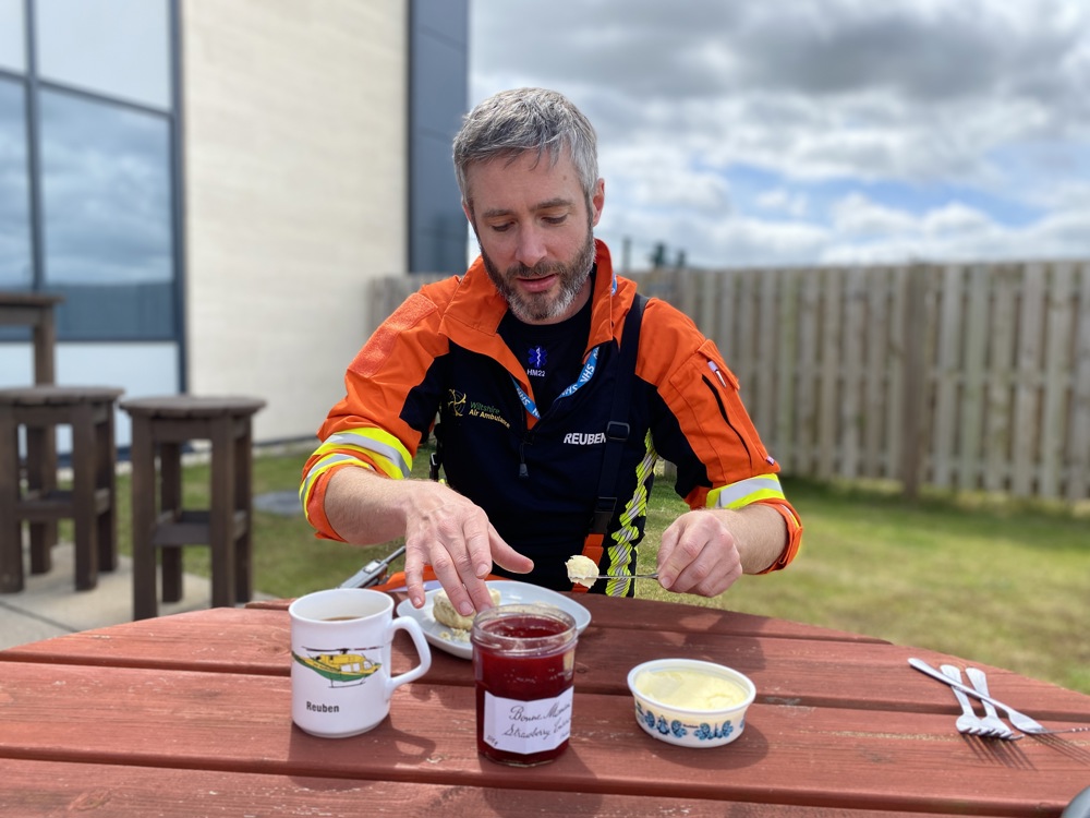 A doctor, wearing an orange flight suit, scooping clotted cream and putting it on a scone