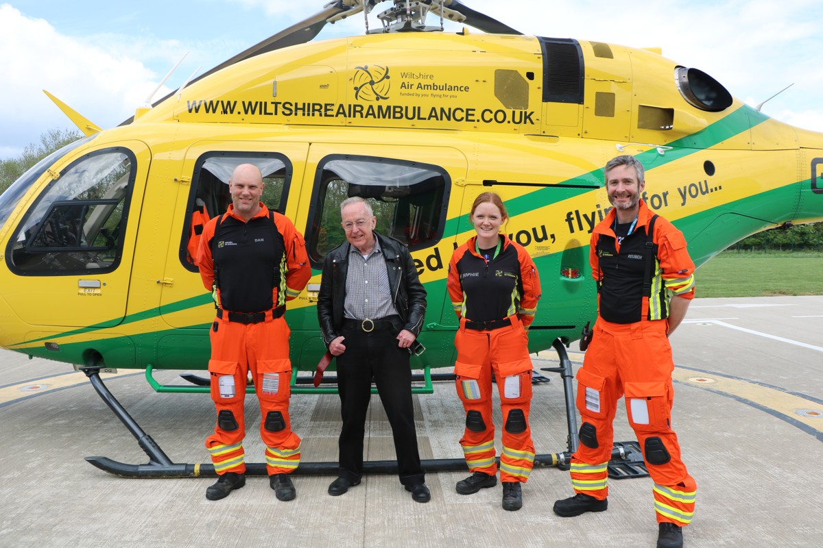 Patient Martyn Dormer standing in front of the helicopter with critical care paramedics Dan and Sophie, and doctor Reuben who are wearing orange flight suits,