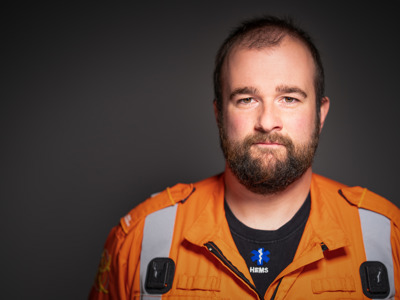 Critical care paramedic James Hubbard headshot photo wearing an orange flight suit on a black background.