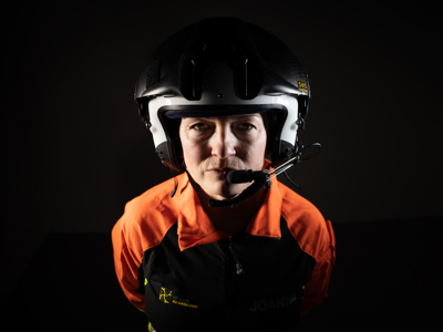 Critical care paramedic Jo Gilbert wearing a flight suit and helmet looking on a black background.