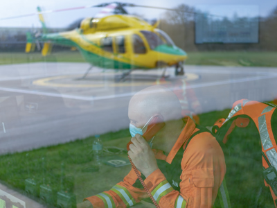 Critical care paramedic Dan Tucker answering the phone in the flight room overlooking the helipad with the Wiltshire Air Ambulance helicopter in the window reflection.