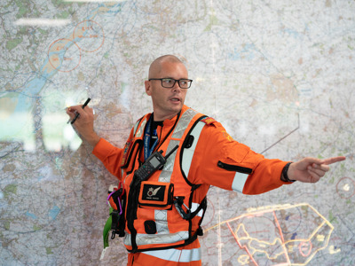 Paramedic Paul Rock standing in front of large map in Wiltshire Air Ambulance's Ops room