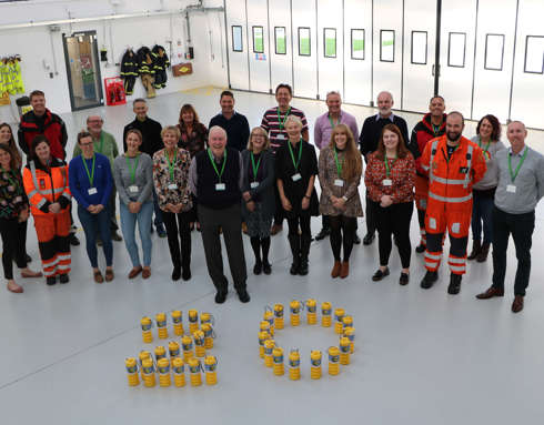 A photo of charity team members with yellow collection tins arranged in the number 20.