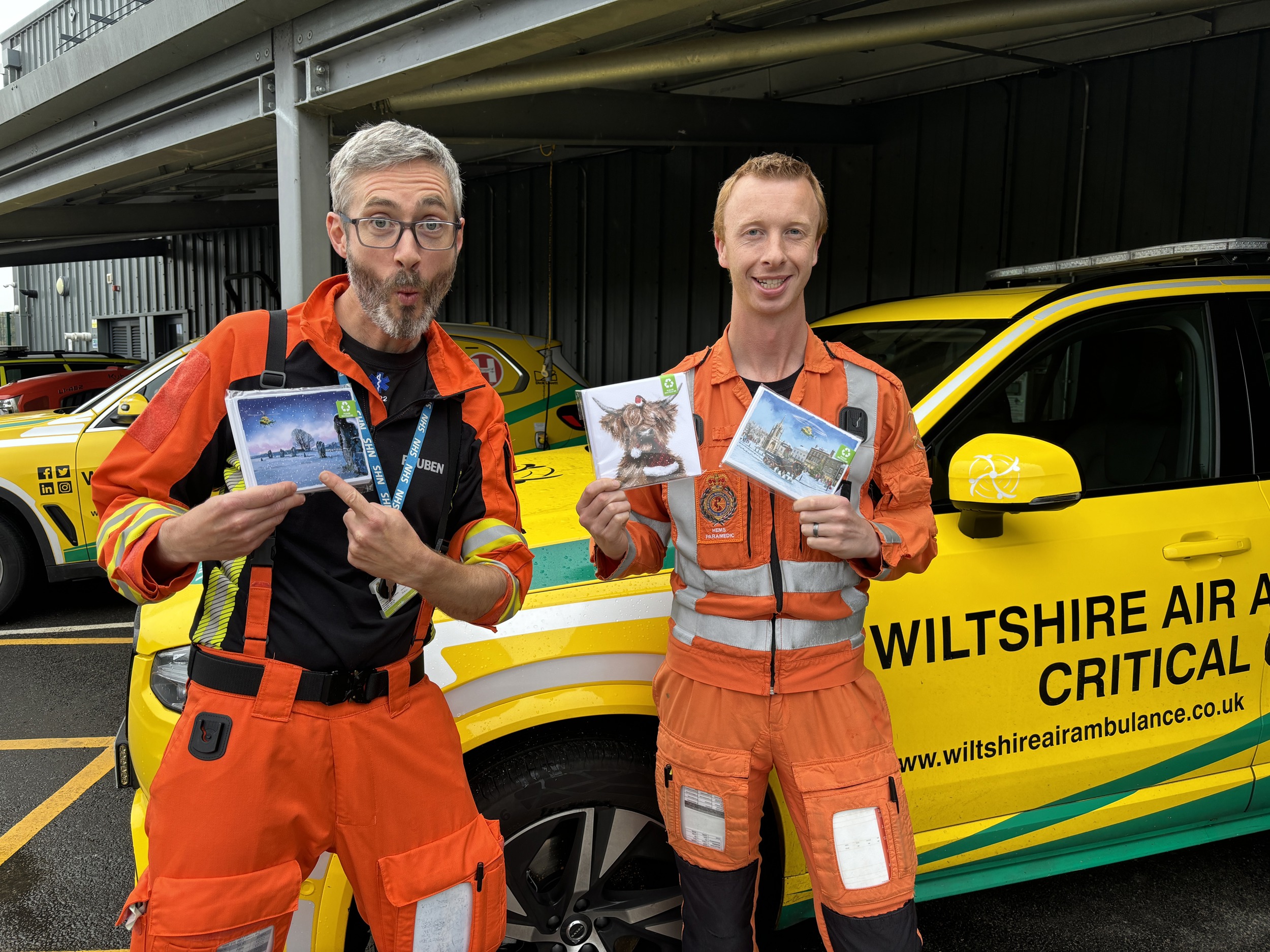 Two medical professionals wearing orange flight suits holding packs of christmas cards