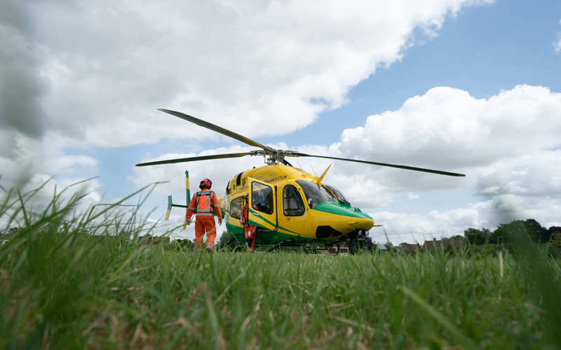 A photo of the yellow and green Bell-429 helicopter in a grassy field featuring two critical care paramedics.