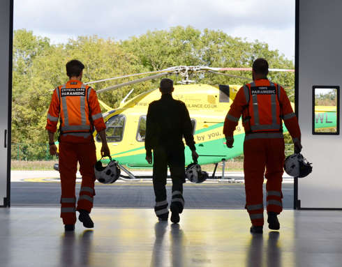 Two paramedics and a pilot walking towards the helicopter from inside the hangar.