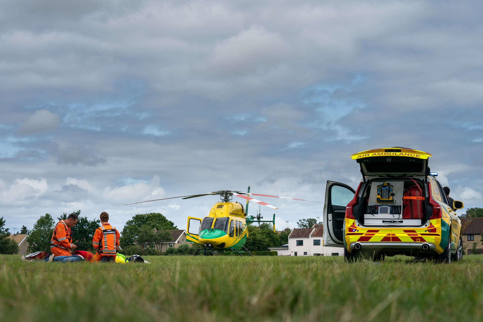 Two paramedics performing a staged incident in a field, with the Wiltshire Air Ambulance yellow and green helicopter and critical care car