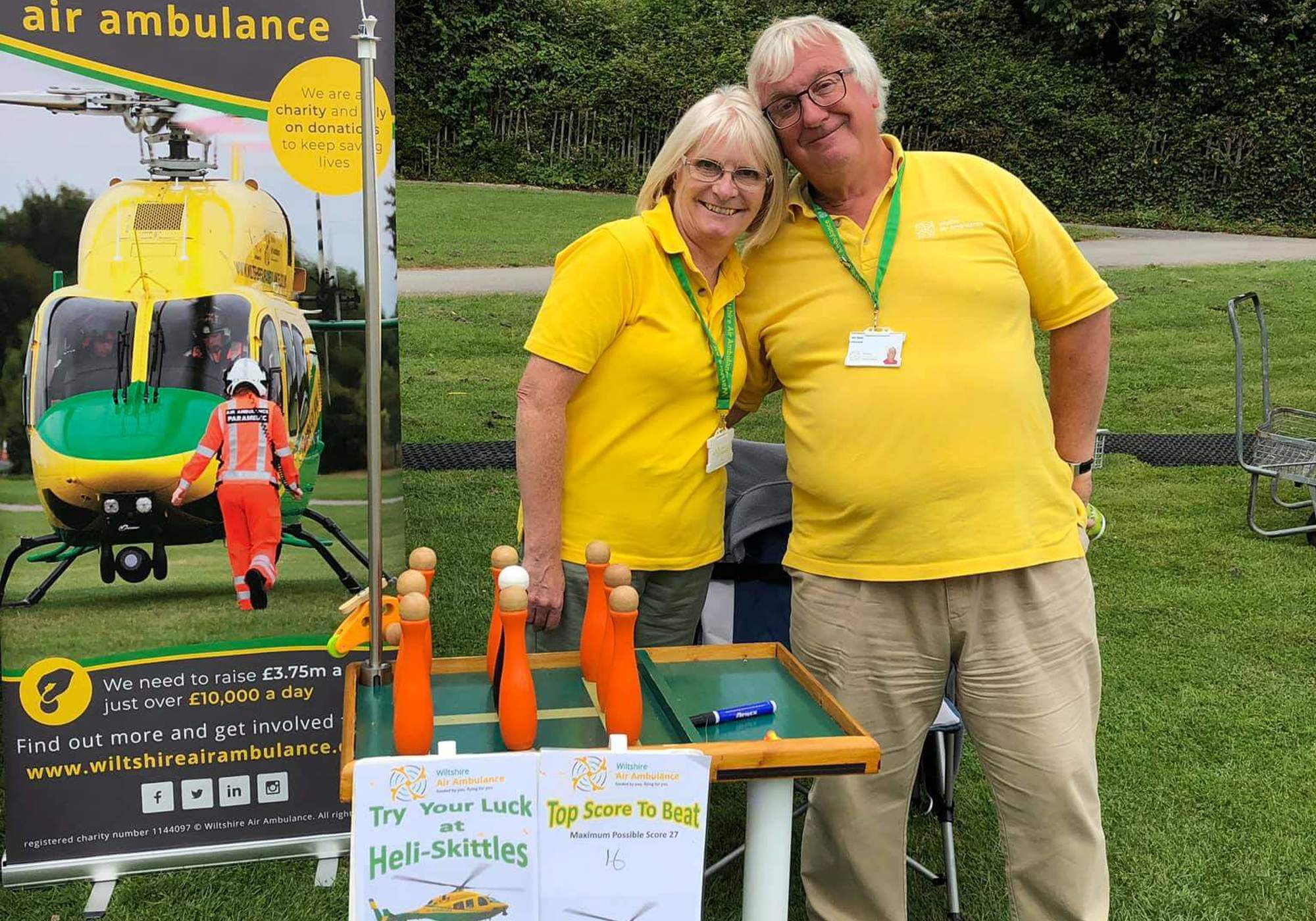 Two volunteers stood in front of a Wiltshire Air Ambulance banner at an event.
