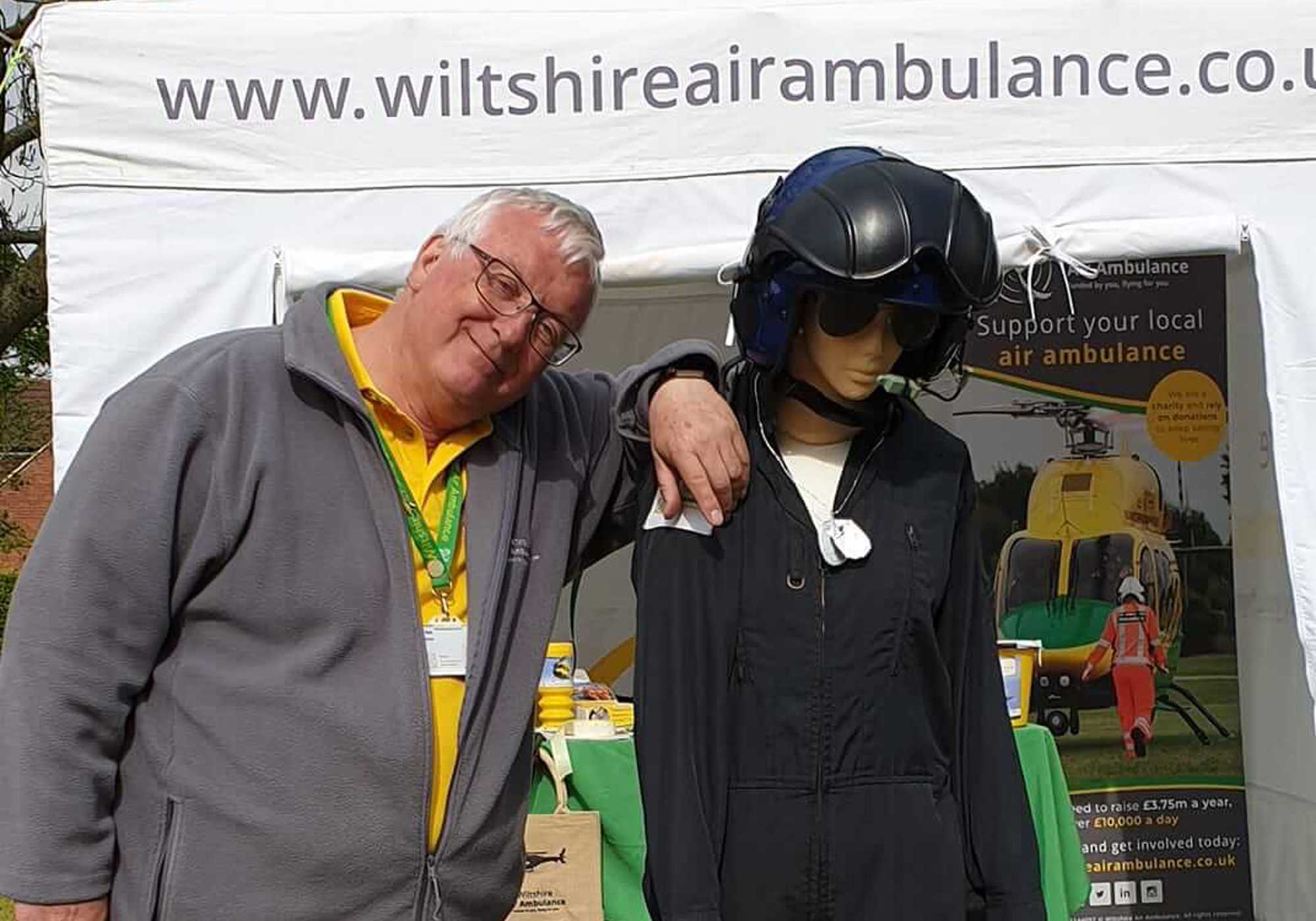 A Wiltshire Air Ambulance volunteer at the Urchfont Scarecrow Festival next to a pilot scarecrow and collection bucket.