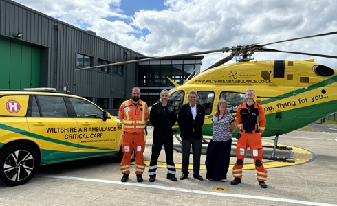 Wiltshire Air Ambulance crew and corporate standing in front of yellow and green helicopter and car