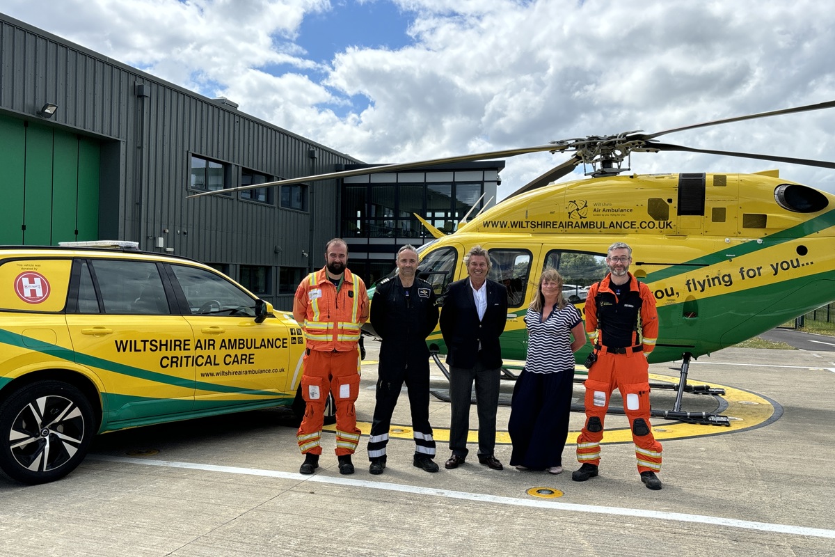 Wiltshire Air Ambulance crew and corporate standing in front of yellow and green helicopter and car
