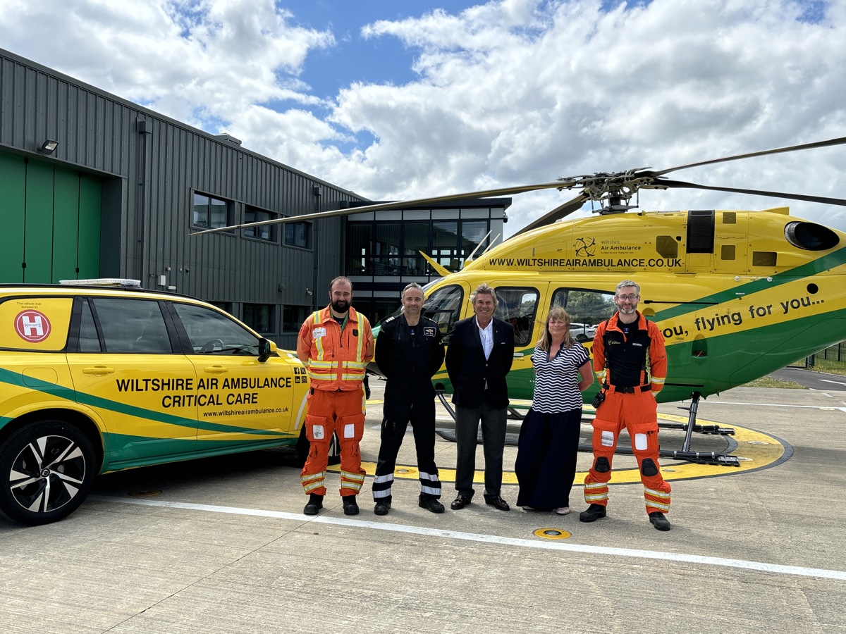 Wiltshire Air Ambulance crew and corporate standing in front of yellow and green helicopter and car