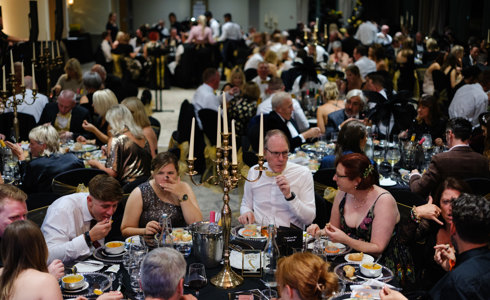 A group of people sitting around tables wearing black and gold