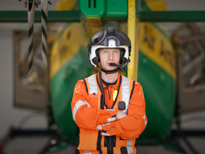 Critical care paramedic Craig Wilkins wearing a flight helmet in front of the airbase hanger and tail rotor of the Wiltshire Air Ambulance helicopter.