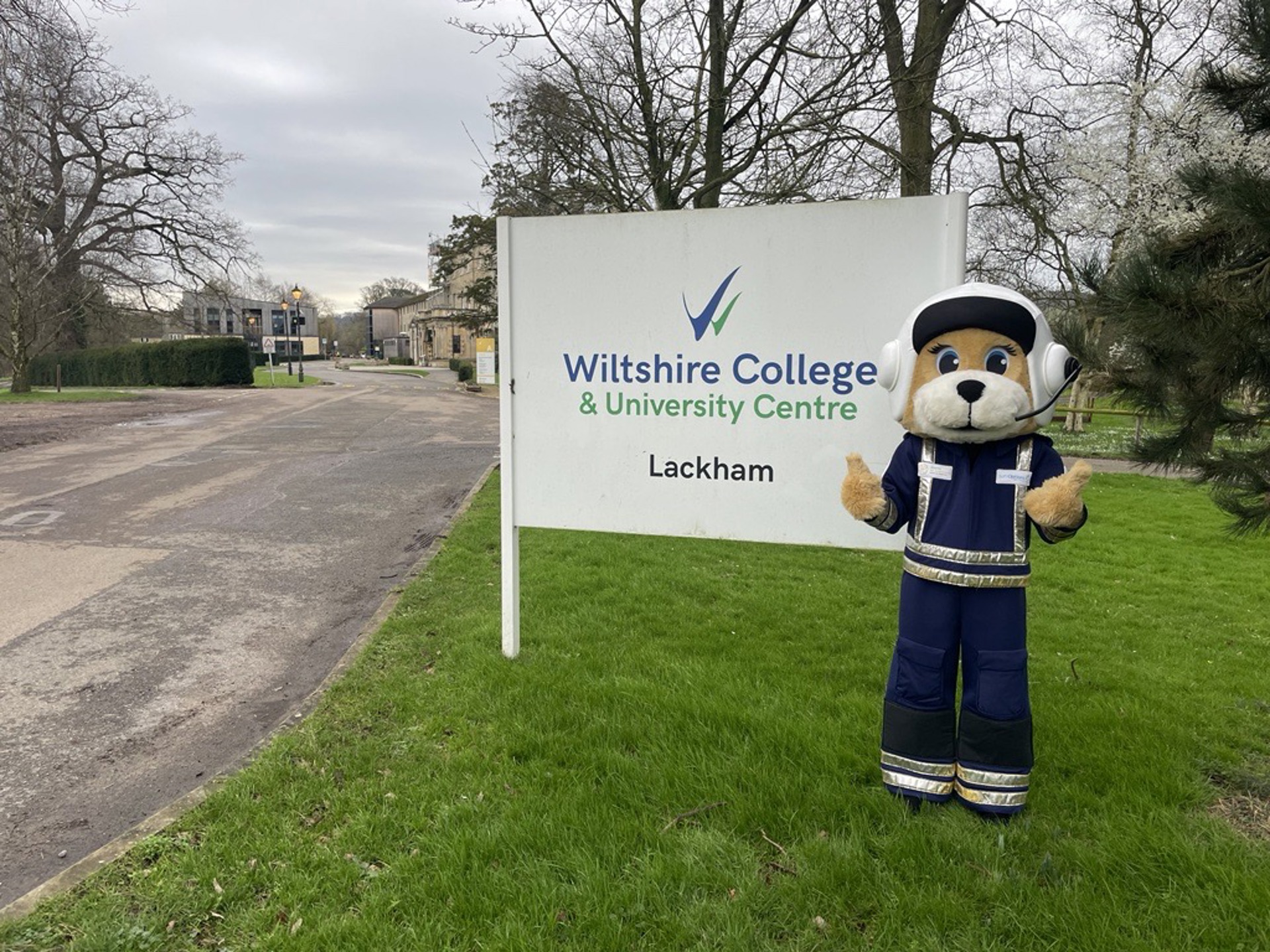 A photo of a bear mascot standing with a sign saying Wiltshire College