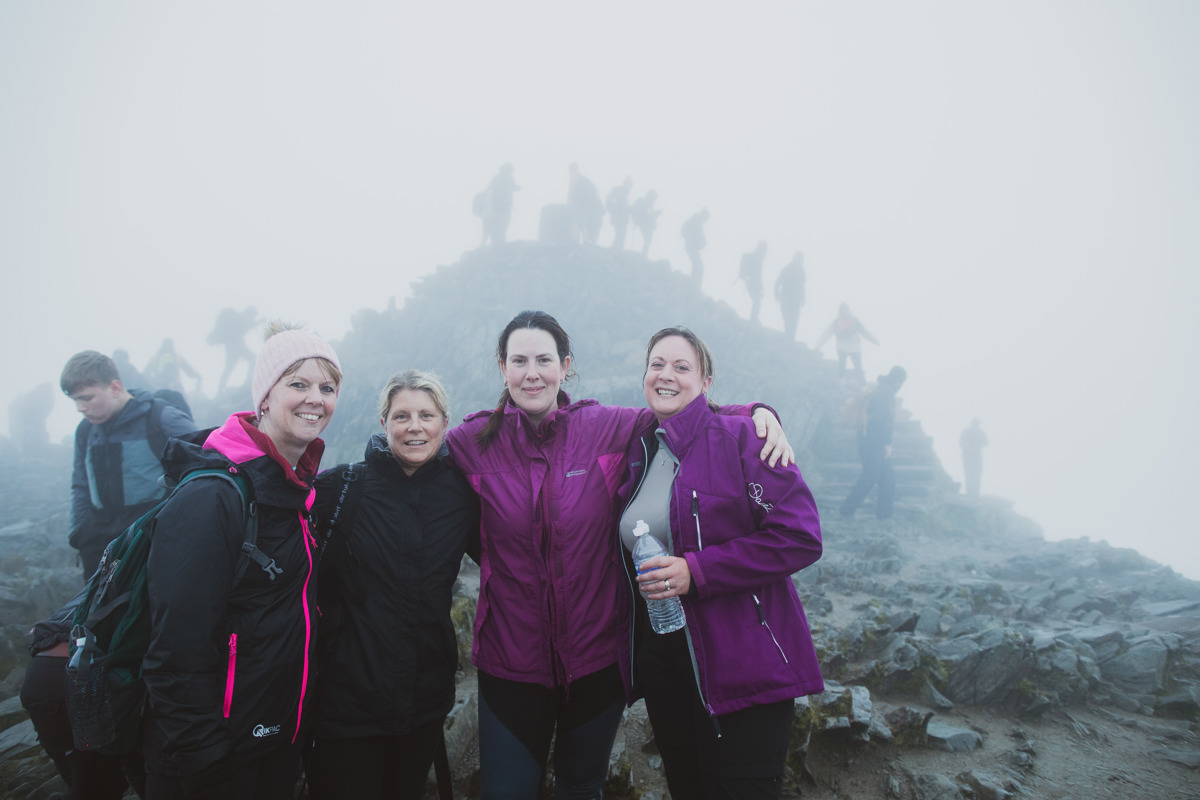 A group of 4 women posing for a photo at the top of Mount Snowdon