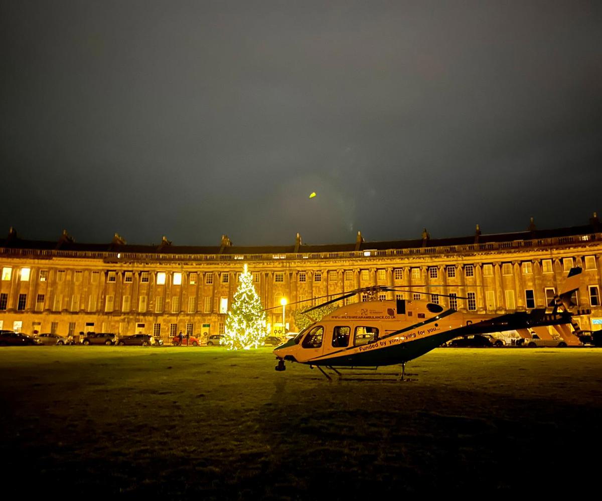 Wiltshire Air Ambulance landed at Royal Crescent, Bath at night, in front of a lit christmas tree