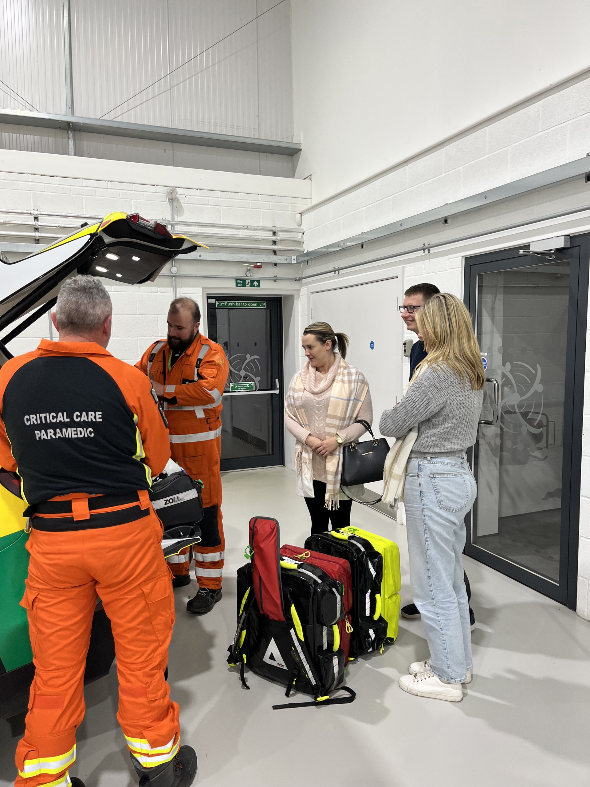 A critical care paramedic wearing orange showing people kit from the back of a critical care car